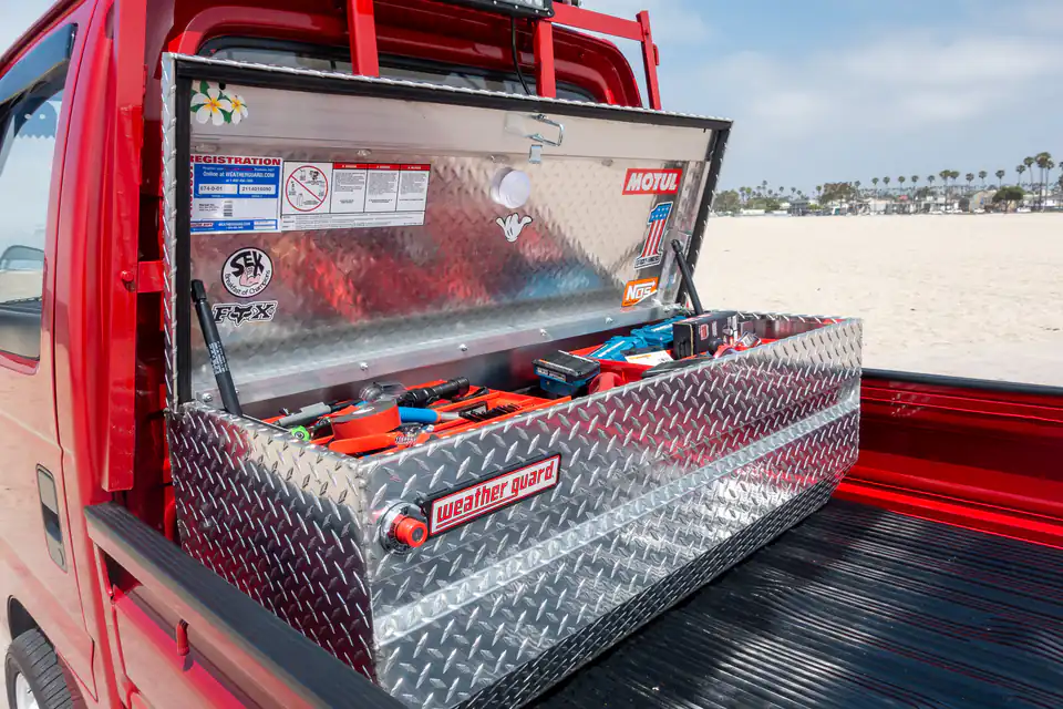 Open diamond plate toolbox in the bed of a red Honda Acty Kei Truck