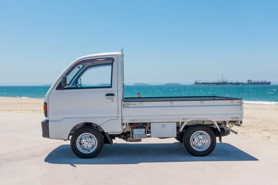 Side profile of a white Mitsubishi Minicab Kei Truck on the beach